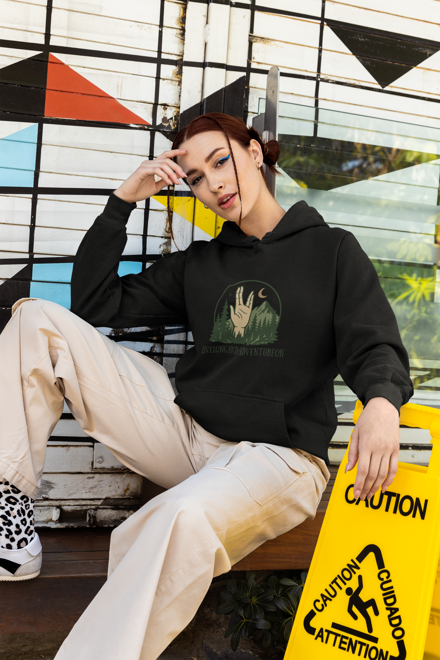 Person wearing a black hoodie with a graphic design, sitting on a bench in front of a colorful geometric wall.