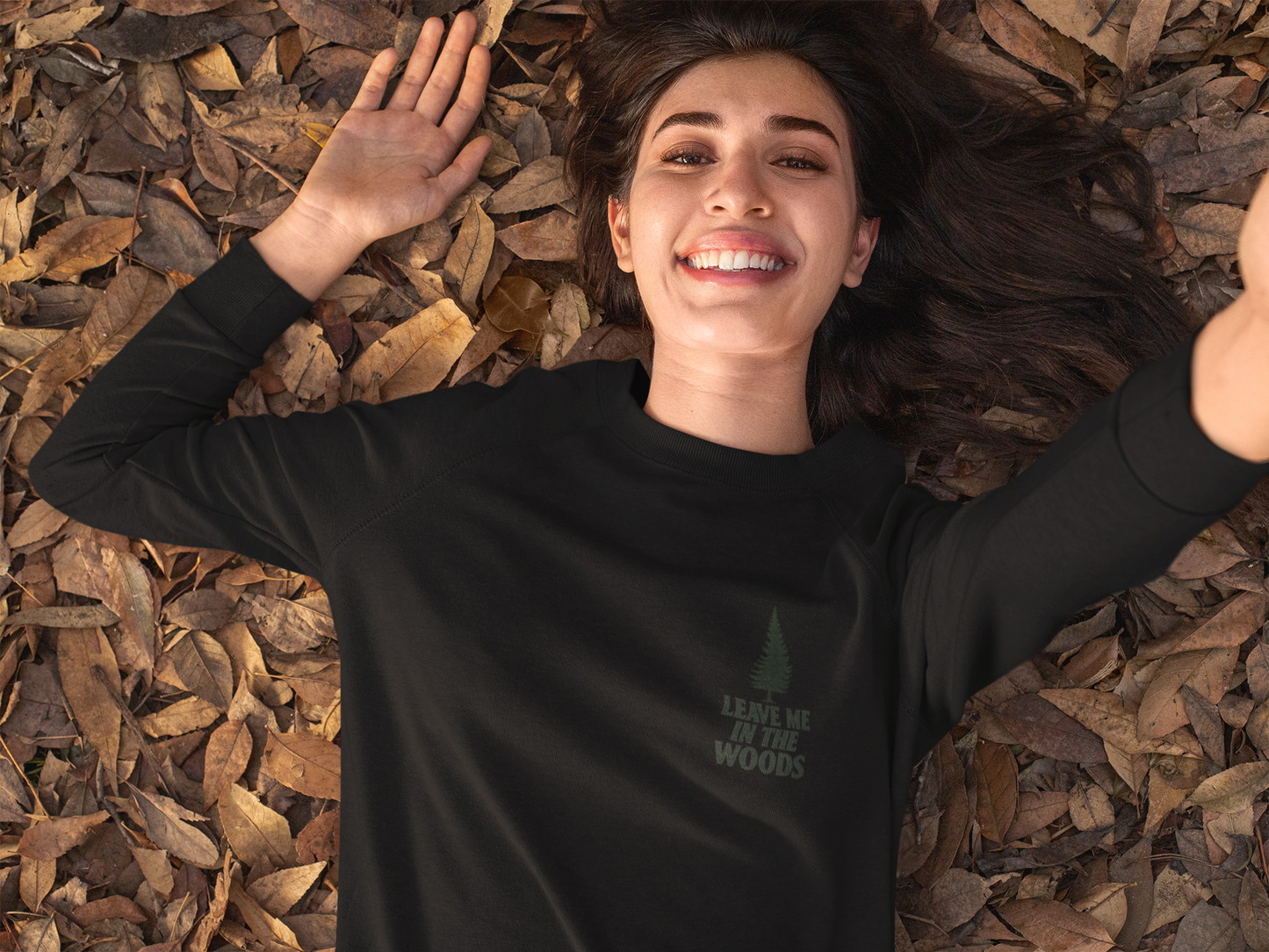 Person wearing a black sweatshirt with text lying on dry leaves
