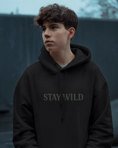 Person wearing a black hoodie with 'STAY WILD' text against a dark background