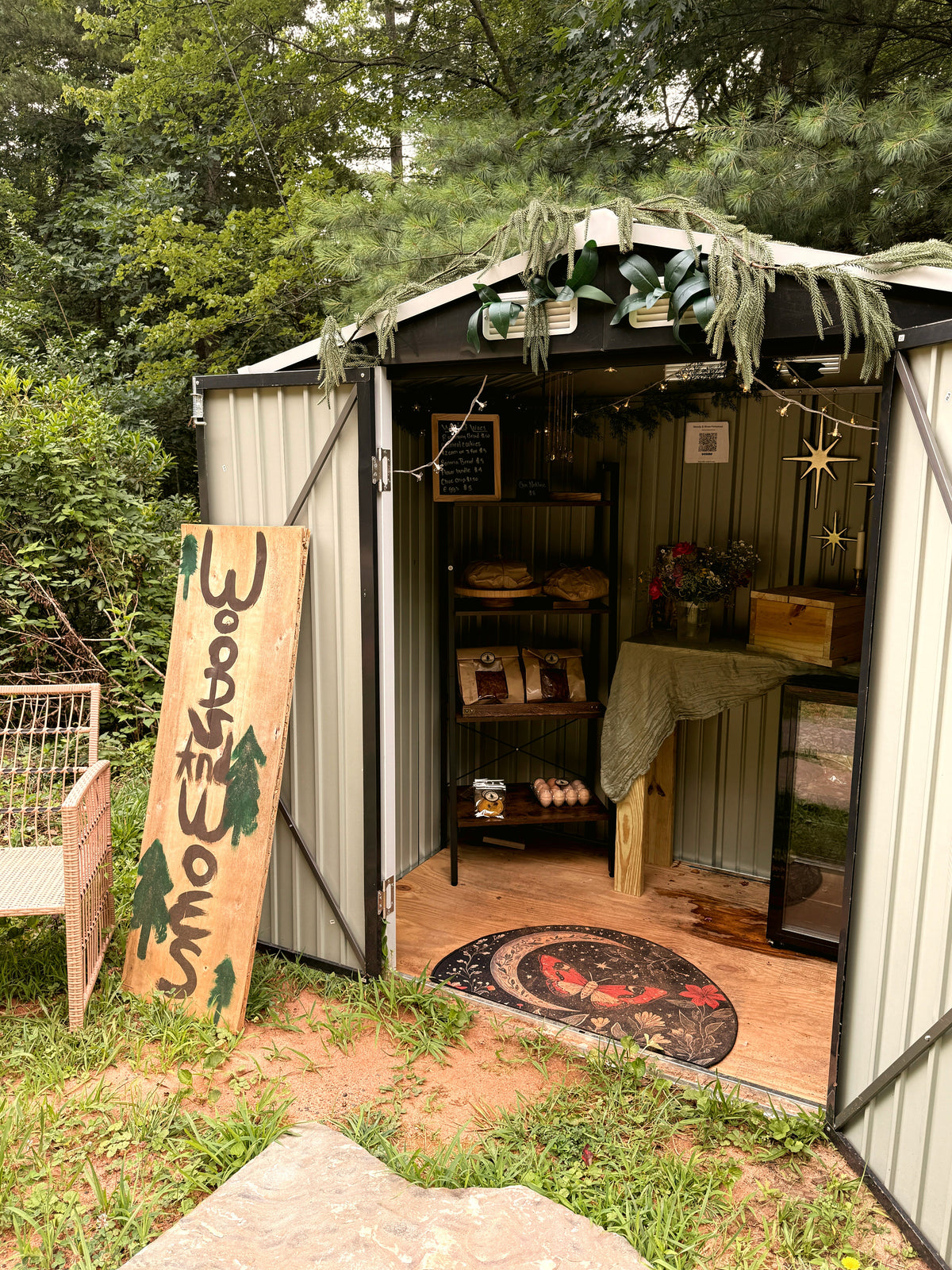 Small farmstand surrounded by trees with a Woods & Woes sign by the entrance