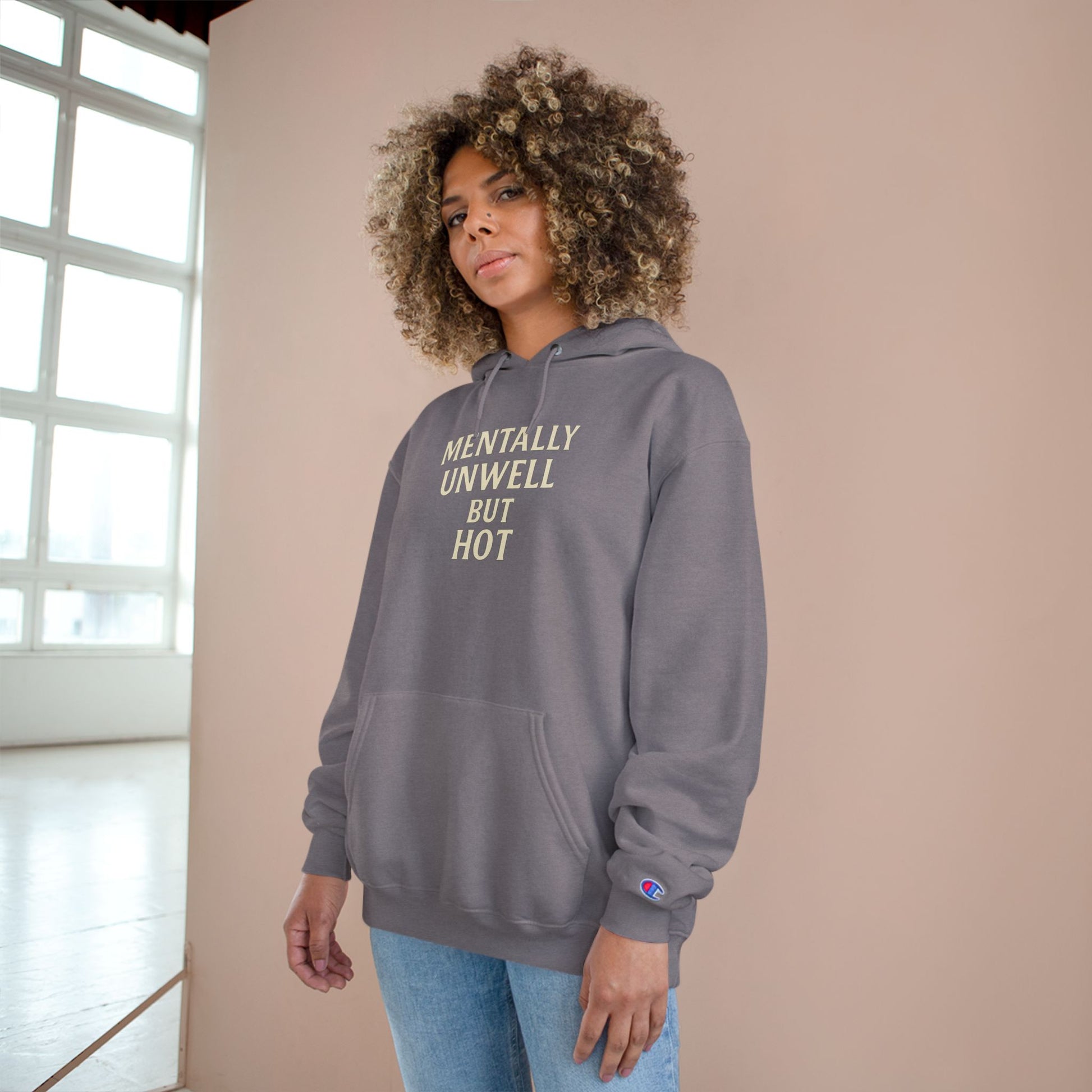 Person wearing a gray hoodie with text, standing indoors against a beige wall.