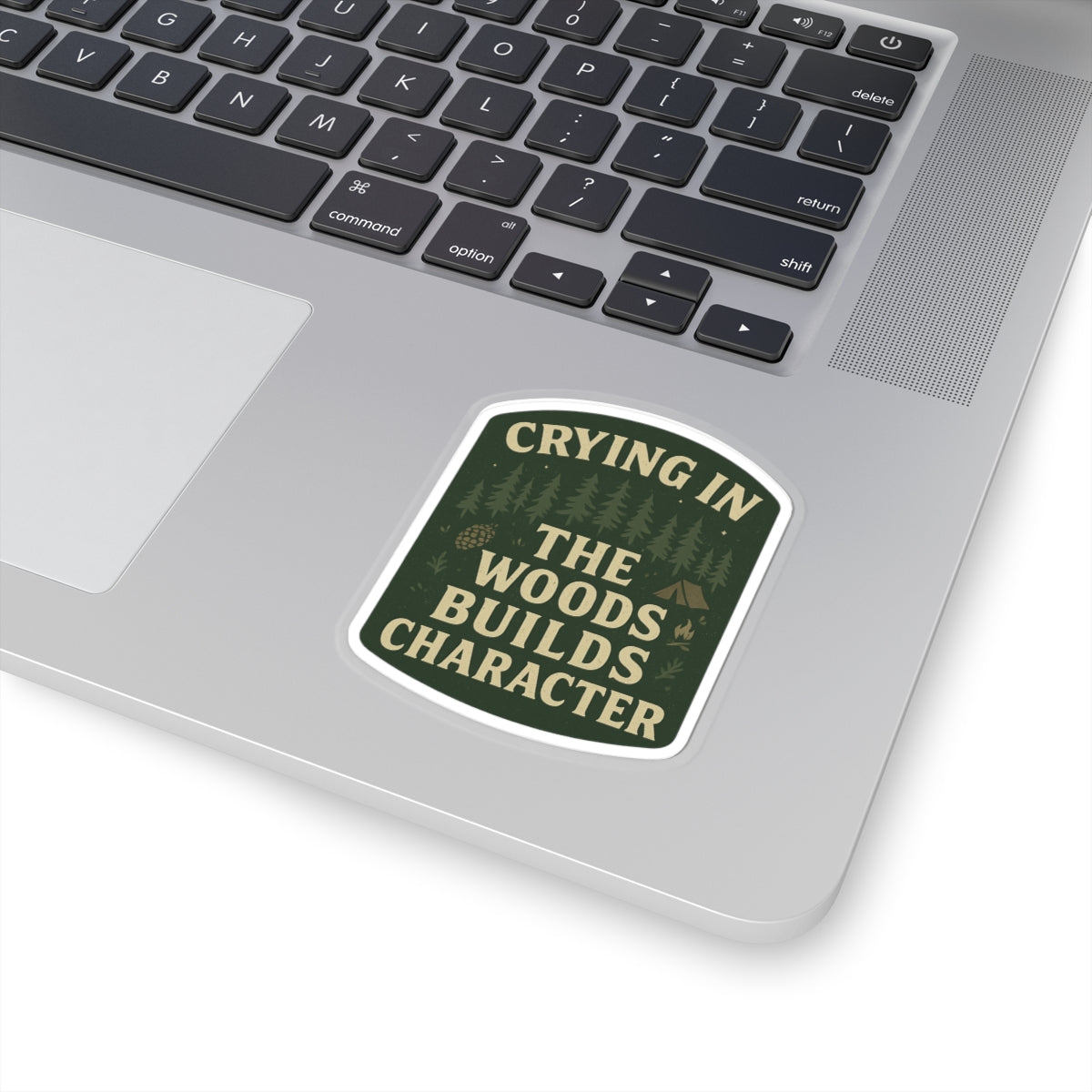 Laptop with a sticker reading 'Crying in the woods builds character' on a white background
