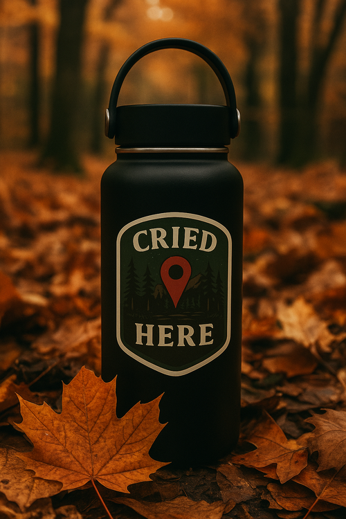 Black water bottle with 'CRIED HERE' label on a forest floor with autumn leaves