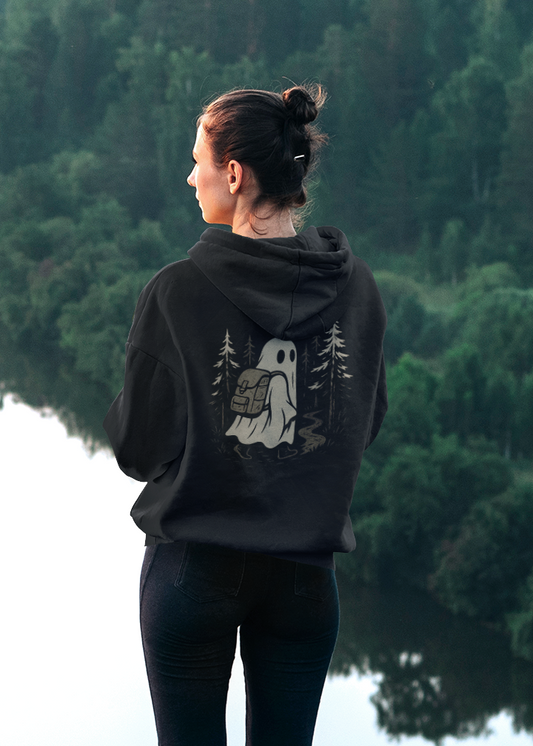 Women in black hoodie with ghost hiking design, standing by a forest lake. 
