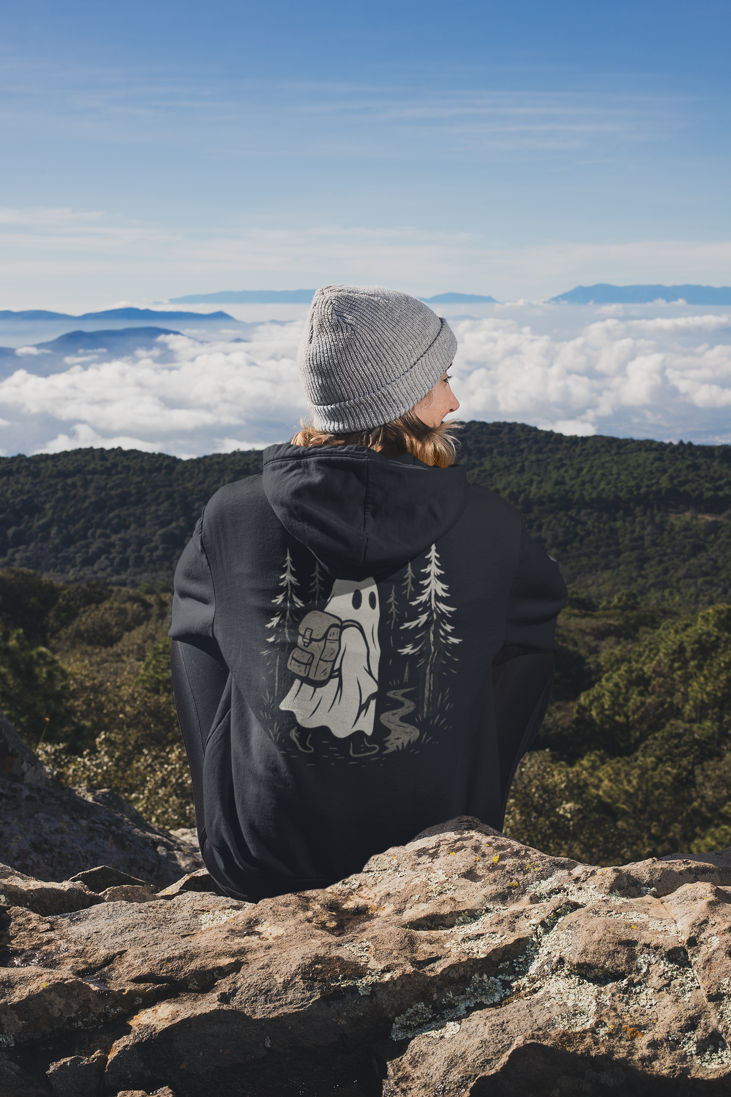 Person wearing a black hoodie with a nature design, standing on a mountain overlooking a scenic landscape.