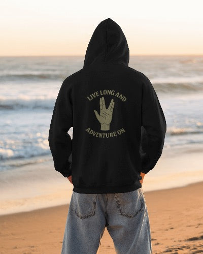 Person wearing a black hoodie with 'Live Long and Adventure On' text on the beach