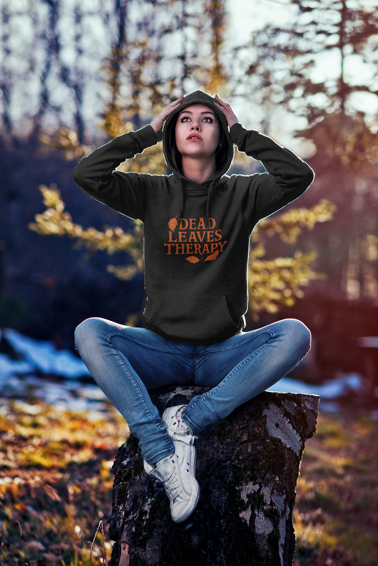 Person wearing a hoodie with text sitting on a rock in a forest setting
