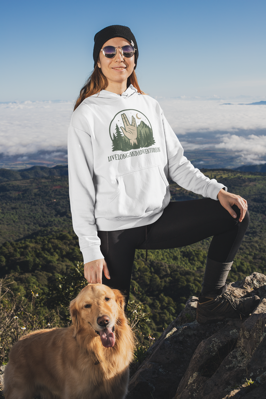 Person wearing a white hoodie with a logo and sunglasses, sitting on a mountain with a dog.